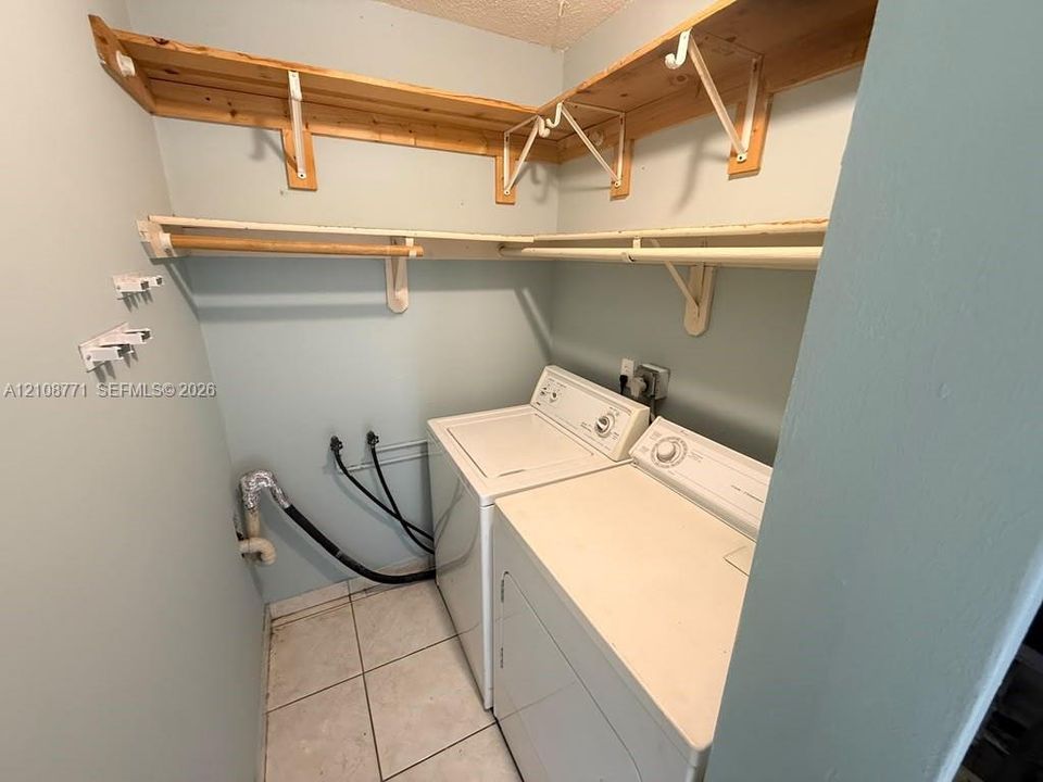 Laundry space featuring ceramic tile flooring, multi-level wood shelving, and dual clothing rods