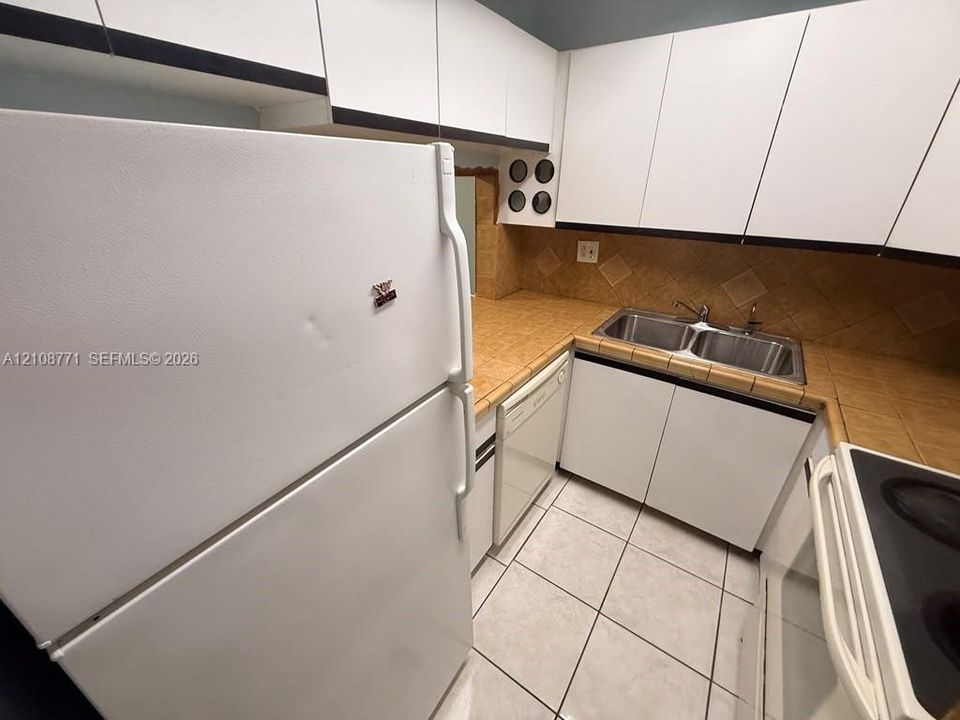 Kitchen featuring white cabinetry, tile countertops with matching backsplash, double-basin stainless steel sink, and ceramic floor tiling