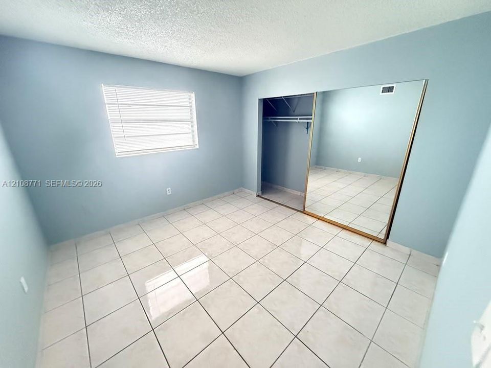 Room featuring neutral-toned tile flooring, light blue wall paint, a single-pane window with horizontal blinds, and a built-in closet with sliding mirrored doors