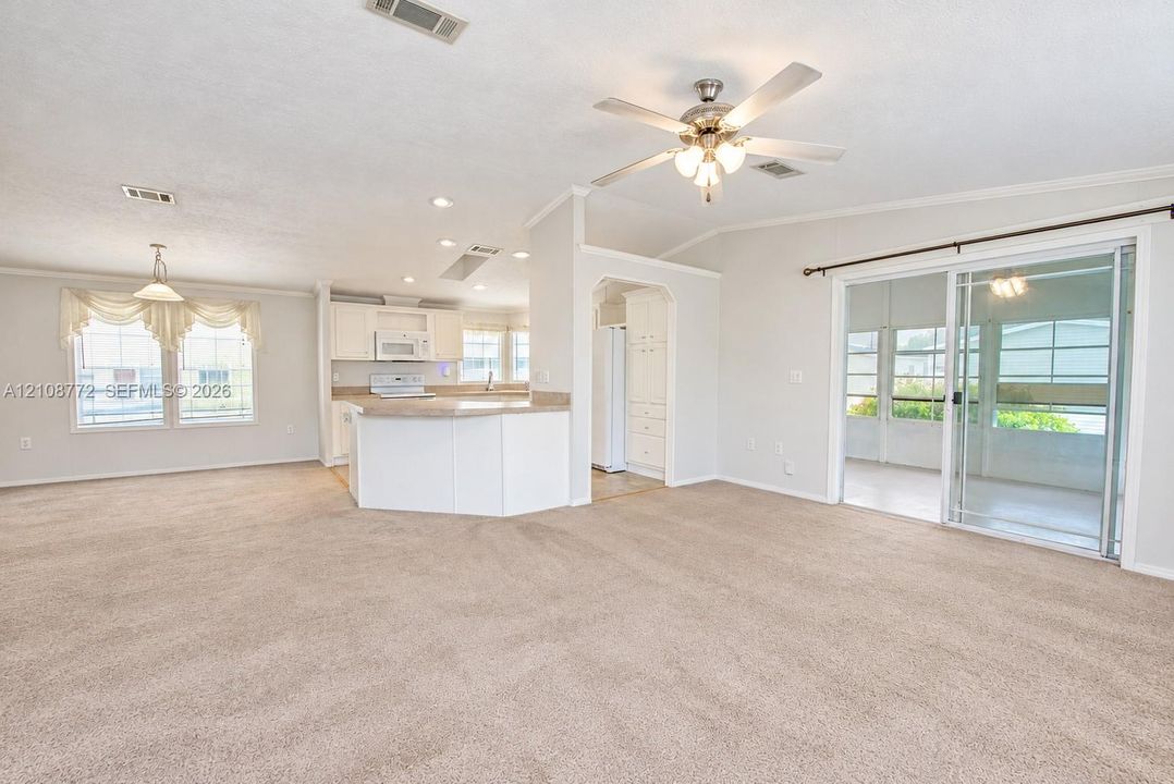 Open-concept interior featuring wall-to-wall carpeting, a kitchen with white cabinetry and a breakfast bar, a ceiling fan with integrated light fixture, and sliding glass doors