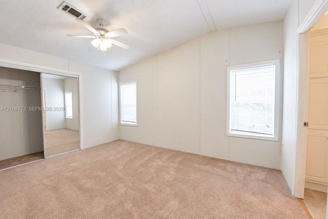 Vaulted ceilings, neutral carpeting, dual-pane windows, ceiling fan with integrated lighting, and mirrored closet doors