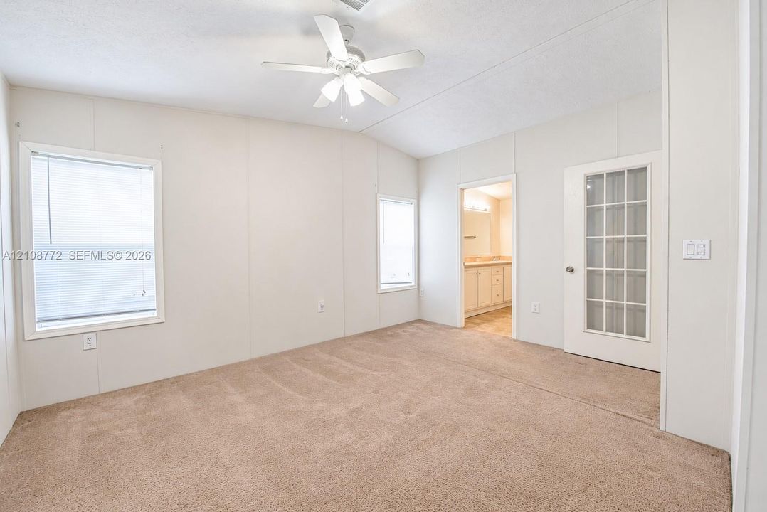 Neutral-toned interior featuring wall-to-wall carpeting, a white ceiling fan with integrated lighting, dual windows, and a glass-paneled entry door