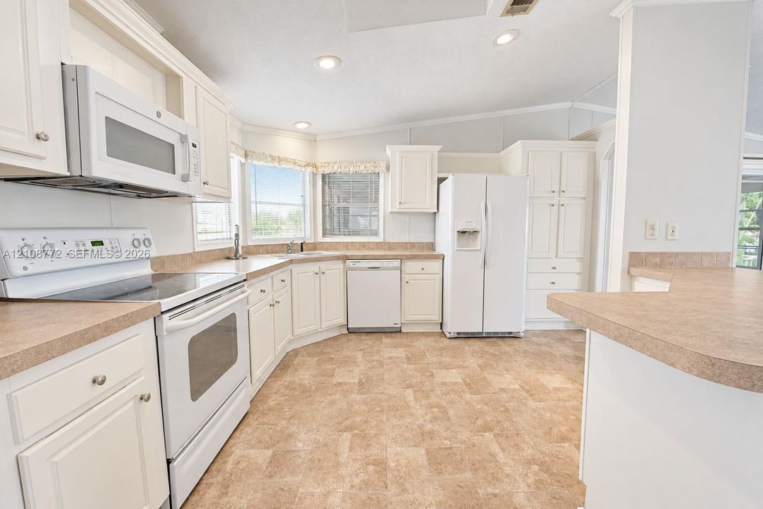 Kitchen featuring white shaker-style cabinetry, a wrap-around laminate countertop, a suite of white appliances, recessed lighting, and tile flooring