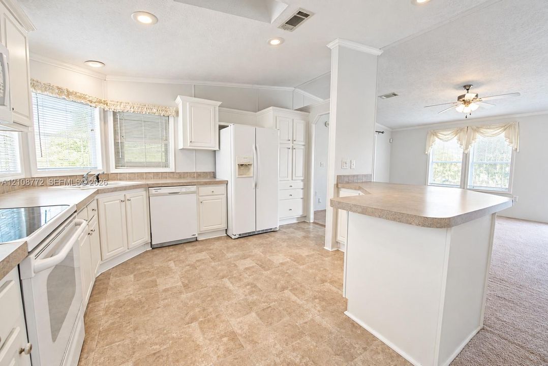 Kitchen featuring white cabinetry, solid-surface countertops, tile-patterned flooring, recessed lighting, and a peninsula with additional surface space
