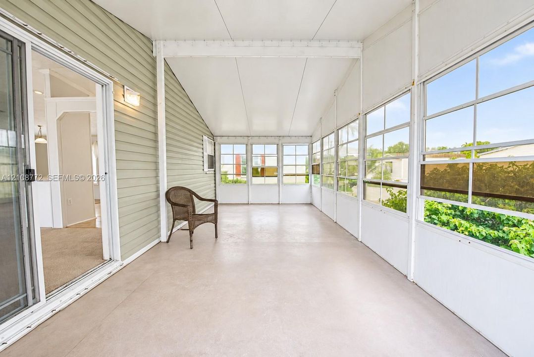 Enclosed porch featuring pale green siding, concrete flooring, sliding glass door, and expansive glass pane windows with grid detailing