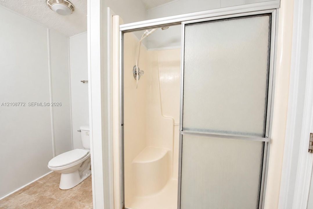 Walk-in shower featuring a built-in seat, sliding frosted glass doors, and a handheld showerhead