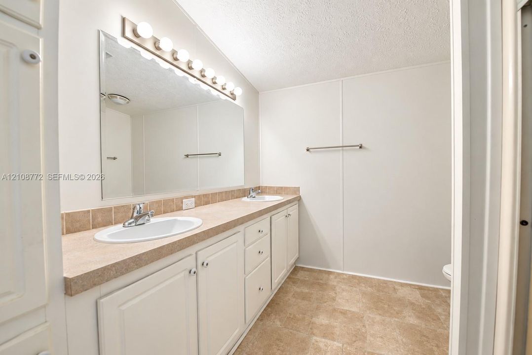 Dual-sink vanity with a solid-surface countertop, full-width vanity mirror, traditional cabinetry, and integrated light fixture