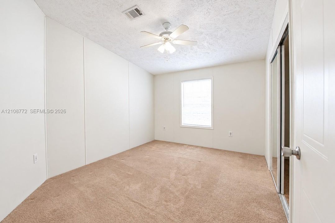 Interior room featuring neutral-tone carpeting, a multi-paneled wall finish, a single-window configuration, and a ceiling-mounted fan with integrated lighting