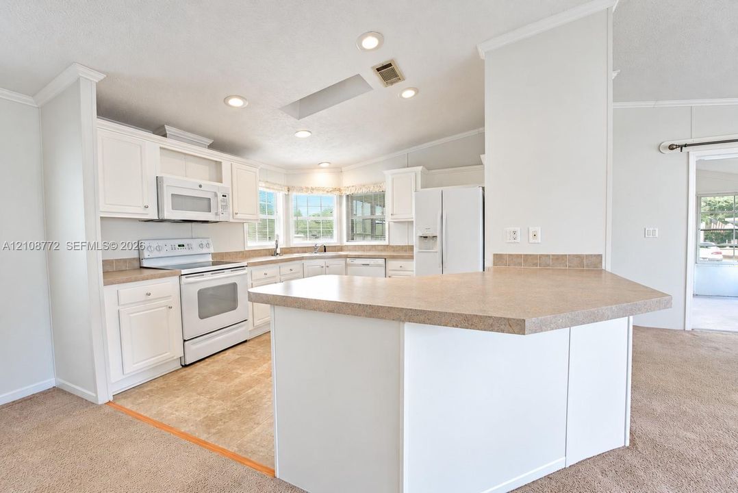 Kitchen featuring white cabinetry, solid-surface countertops, recessed lighting, a built-in skylight, and a peninsula breakfast bar