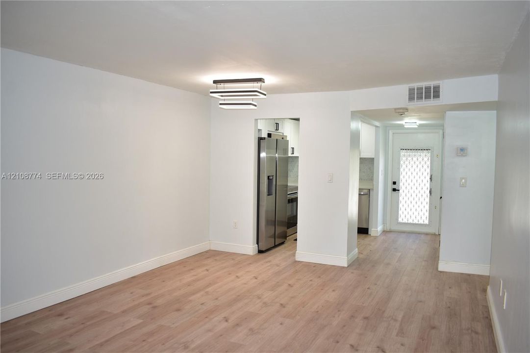 Interior area featuring light wood-finish flooring, a modern multi-tier rectangular flush-mount light fixture, and a stainless steel side-by-side refrigerator