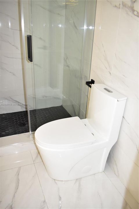 Bathroom featuring floor-to-ceiling large-format tile, glass-enclosed shower, black hexagon floor tile, and a seamless dual-flush toilet