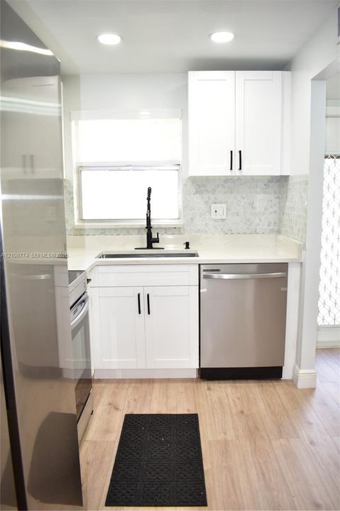 Kitchen featuring white Shaker-style cabinetry, matte black hardware, stainless steel appliances, solid-surface countertops, and wood-finish flooring