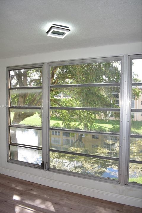Large-pane louvered windows with silver-tone metal framing, wood-finish flooring, and a modern geometric square flush-mount ceiling fixture