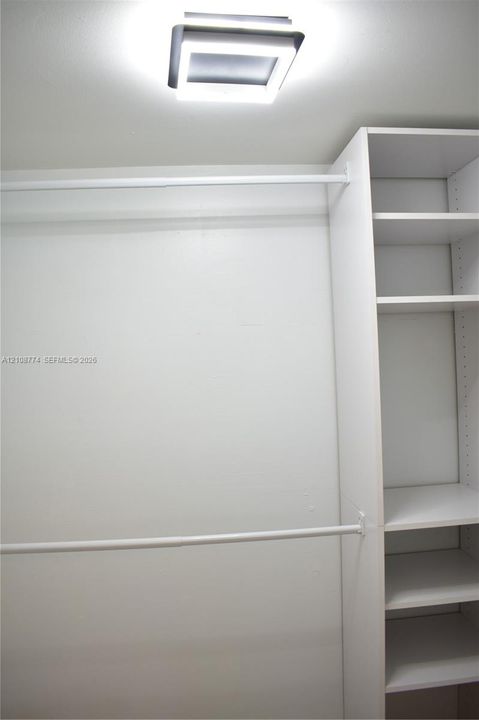 Storage area featuring dual metal garment rods and white built-in shelving, complemented by a square flush-mount LED fixture