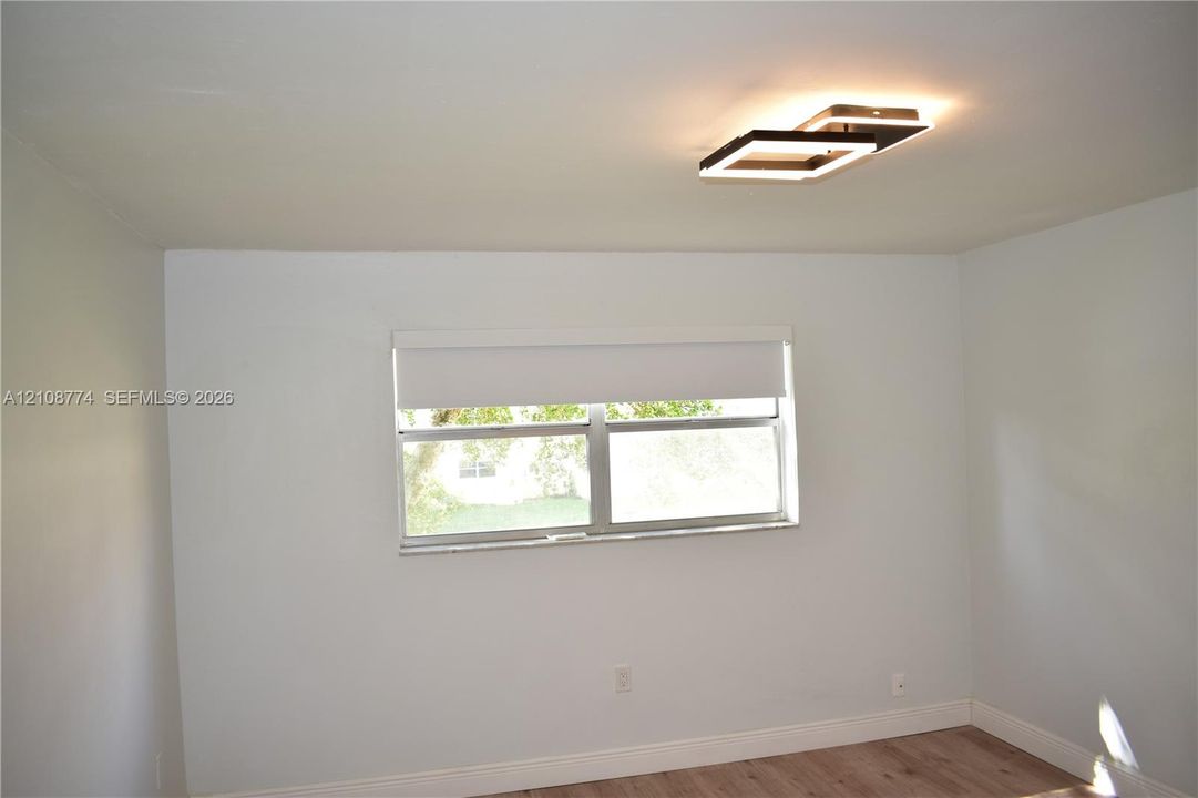 Room featuring wood-finish flooring, a modern geometric LED ceiling light fixture, and a window with a retractable roller shade