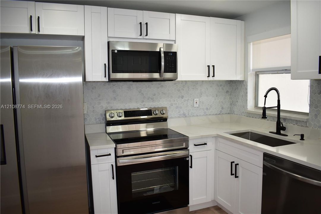 Kitchen featuring white Shaker-style cabinetry with matte black hardware, stainless steel appliances, white countertops, a patterned tile backsplash, and a matte black gooseneck faucet