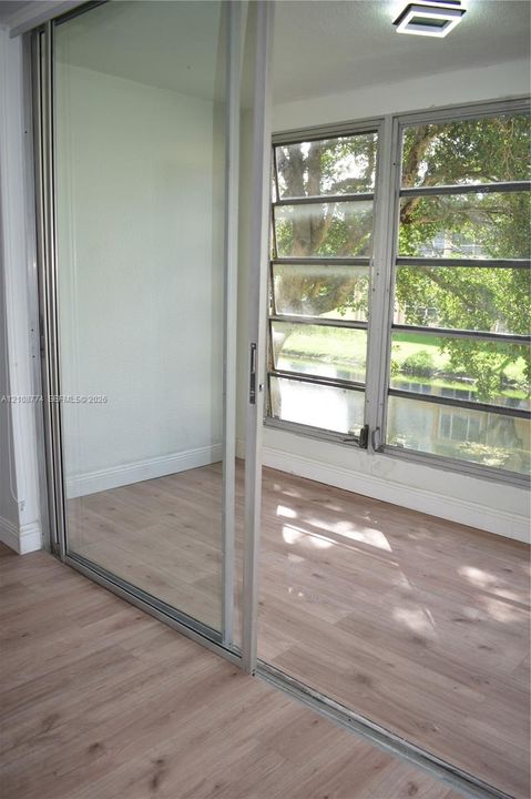 Sliding glass partition with a metal frame, light-toned wood-finish flooring, and multi-pane windows providing an outlook onto mature trees and water