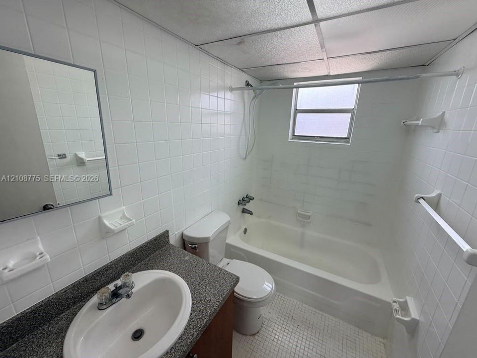 Bathroom featuring white wall tile, a tub-shower combination, a stone-finish countertop, an integrated oval sink, and a drop ceiling