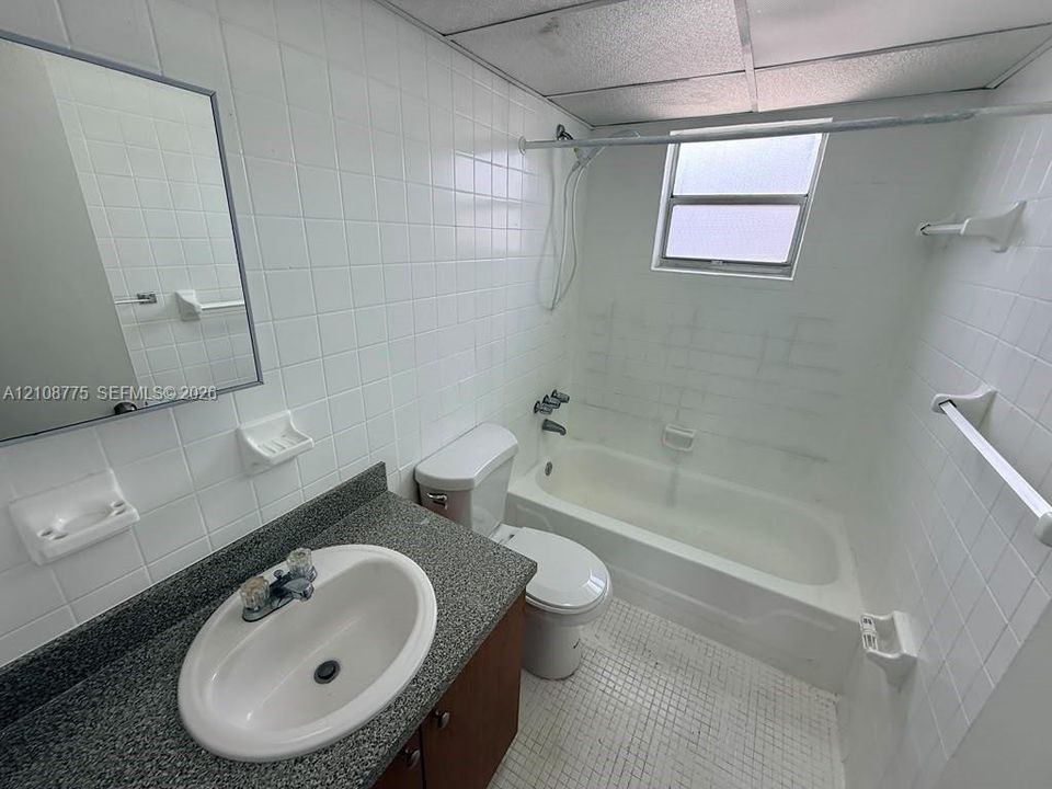 Bathroom featuring a vanity with a solid-surface countertop, an inset oval sink, a tiled bathtub surround, and a drop ceiling