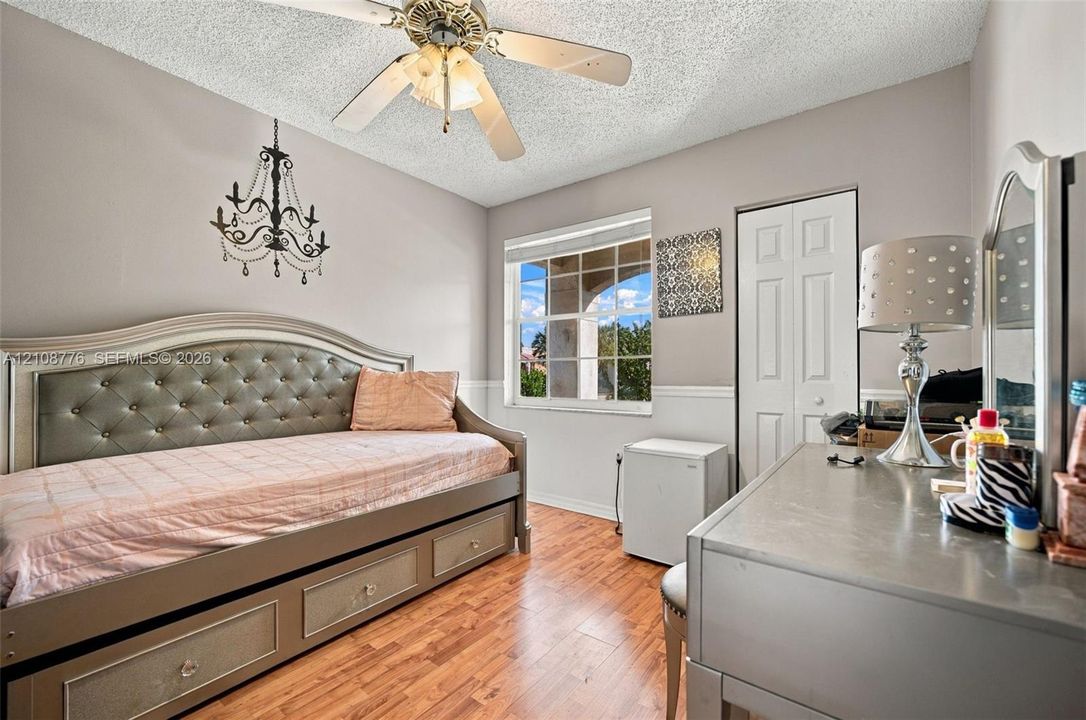 Wood-finish flooring, multi-pane window with grid pattern, decorative hanging chandelier, ceiling fan with integrated lighting, and white bi-fold closet doors