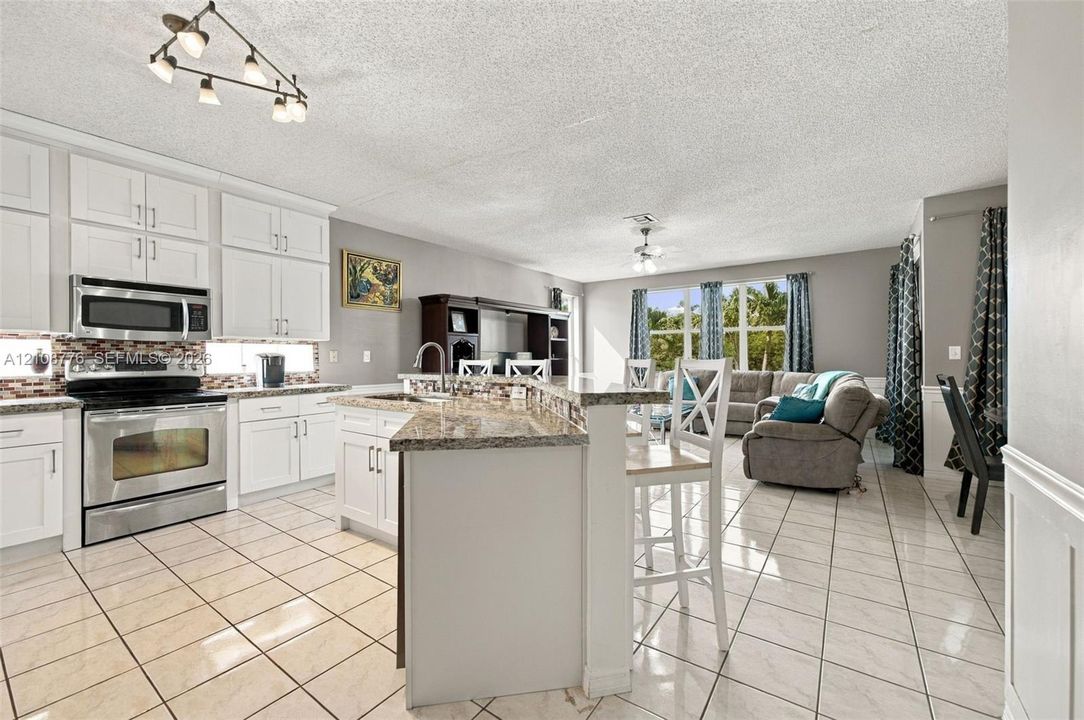 Kitchen featuring white shaker-style cabinetry, stone-finish countertops, stainless steel appliances, a multi-tiered breakfast bar, and tile flooring