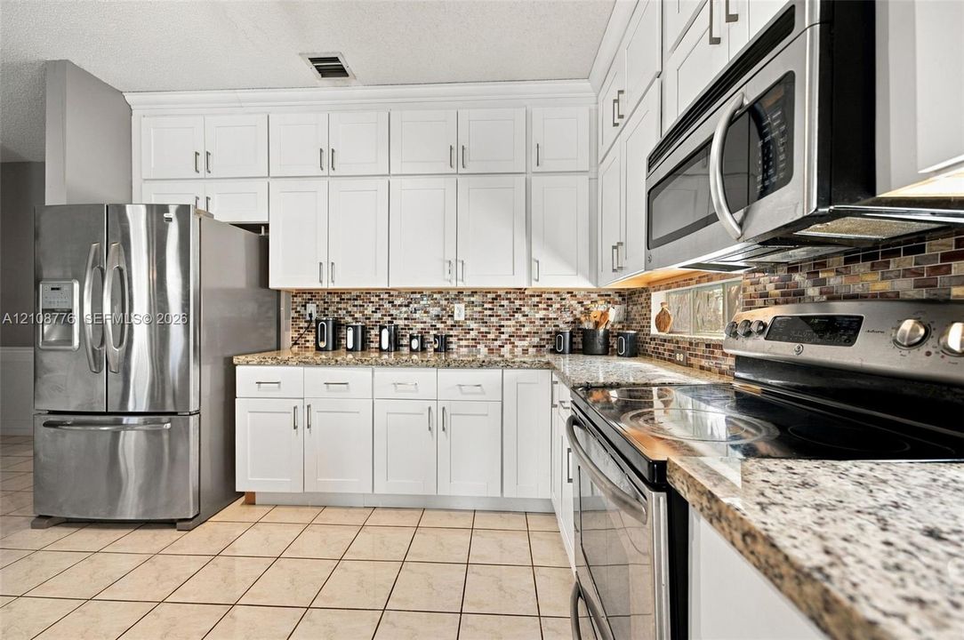 Kitchen featuring white shaker-style cabinetry, stone-finish countertops, stainless steel appliances, and multi-toned glass tile backsplash