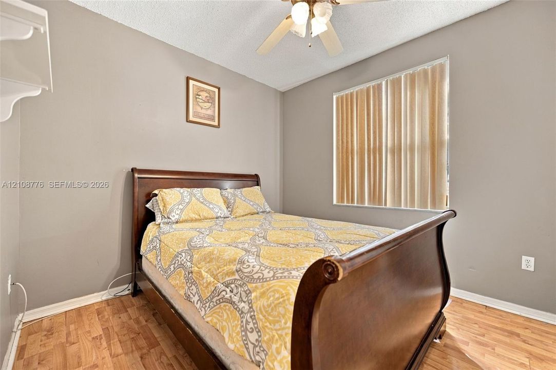 Room featuring wood-finish flooring, a ceiling-mounted fan with integrated lighting, and a window with vertical blinds
