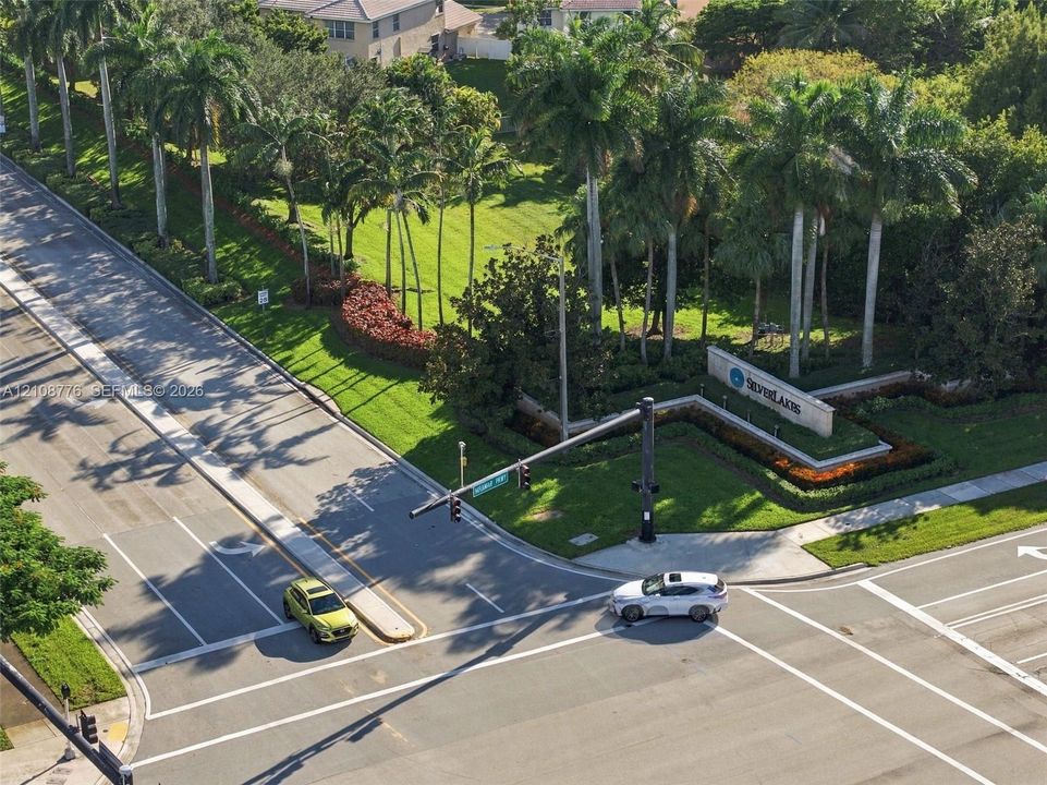 Community entrance featuring mature palm trees, landscaped green space, and prominent stone-finish signage