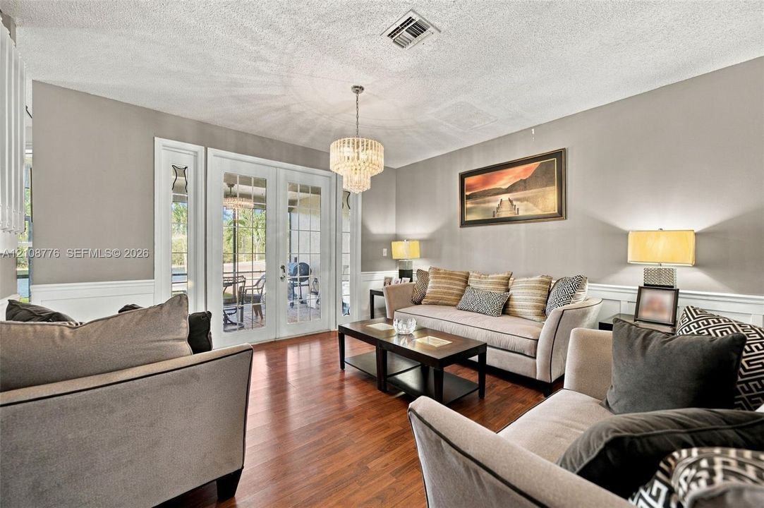Living area featuring wood-finish flooring, multi-pane French doors, a tiered crystal chandelier, and wainscoting