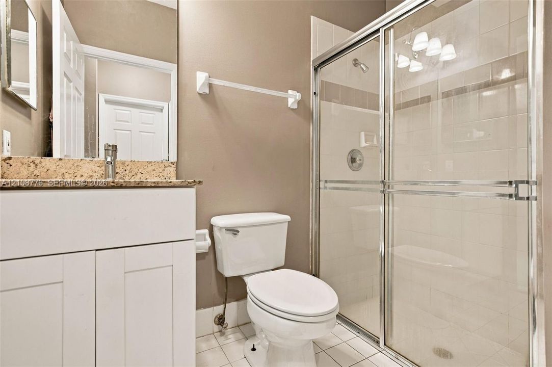 Bathroom featuring a white vanity cabinet with a speckled stone countertop, a glass-enclosed shower with tiled surround, and ceramic tile flooring