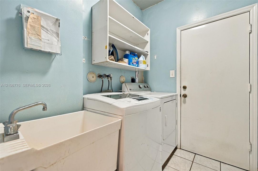 Utility space featuring a basin sink with a chrome faucet, built-in shelving, tiled flooring, and a dedicated exterior access door