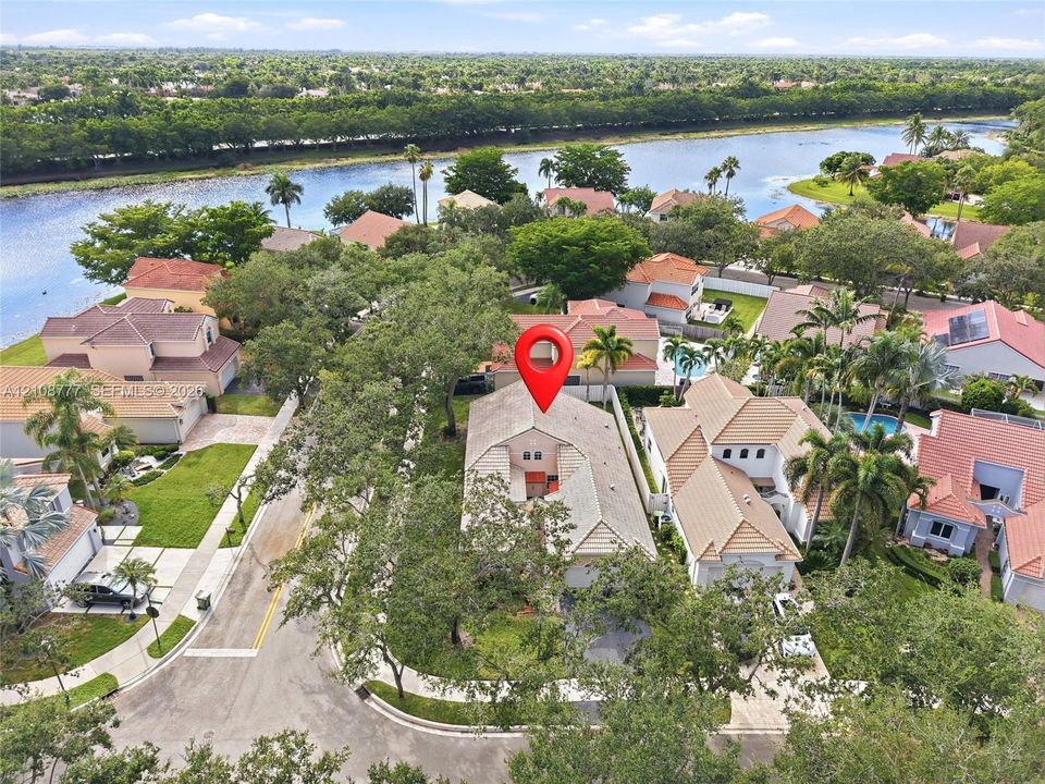 Aerial perspective featuring a multi-story residence with a pitched tile roof, positioned on a corner lot within a waterfront community