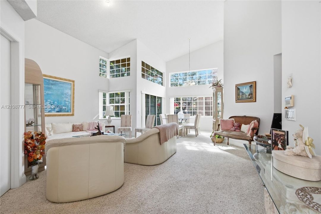 Vaulted ceilings featuring expansive floor-to-ceiling windows with grid-pattern muntins, neutral carpeting, and a central pendant light fixture