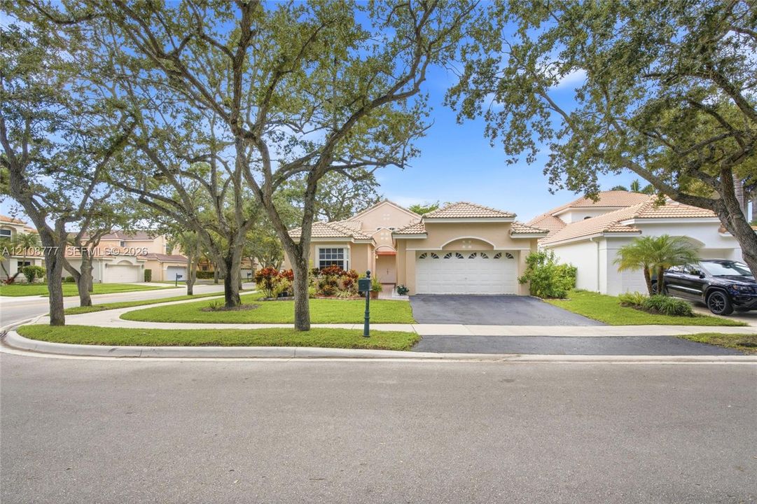 Single-story residence featuring a stucco exterior, tile roofing, an attached two-car garage, and a paved driveway, set on a corner lot with mature landscaping