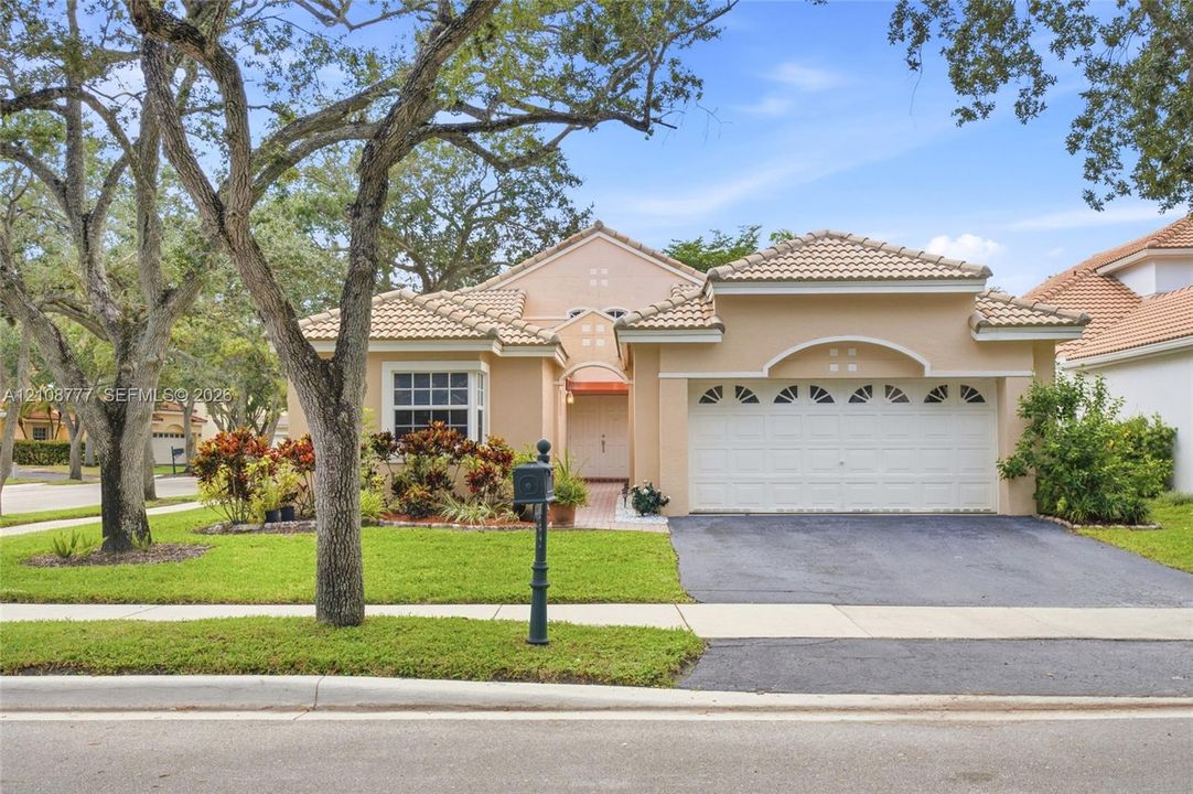 Stucco exterior featuring a tile roof, arched entryway detail, double-car garage, and mature landscape