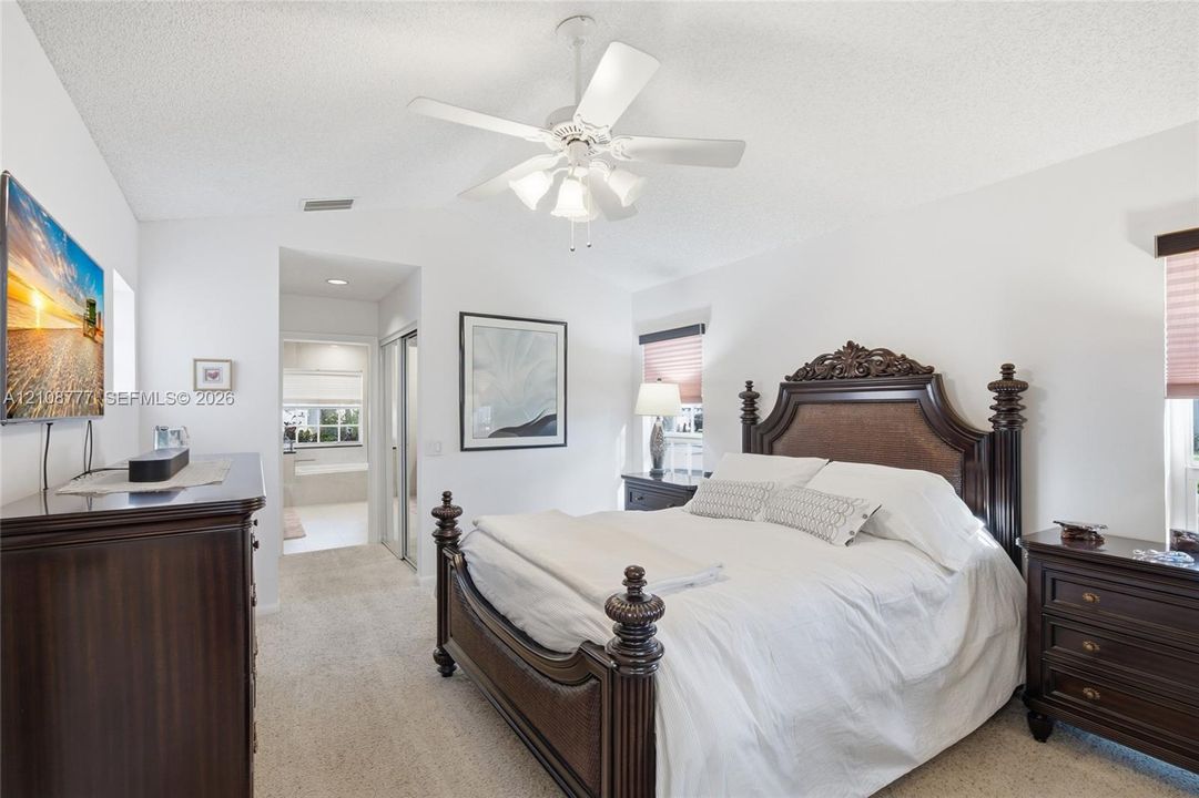 Neutral interior featuring wall-to-wall carpeting, vaulted ceilings, a multi-blade ceiling fan with integrated lighting, and dual-panel sliding closet doors