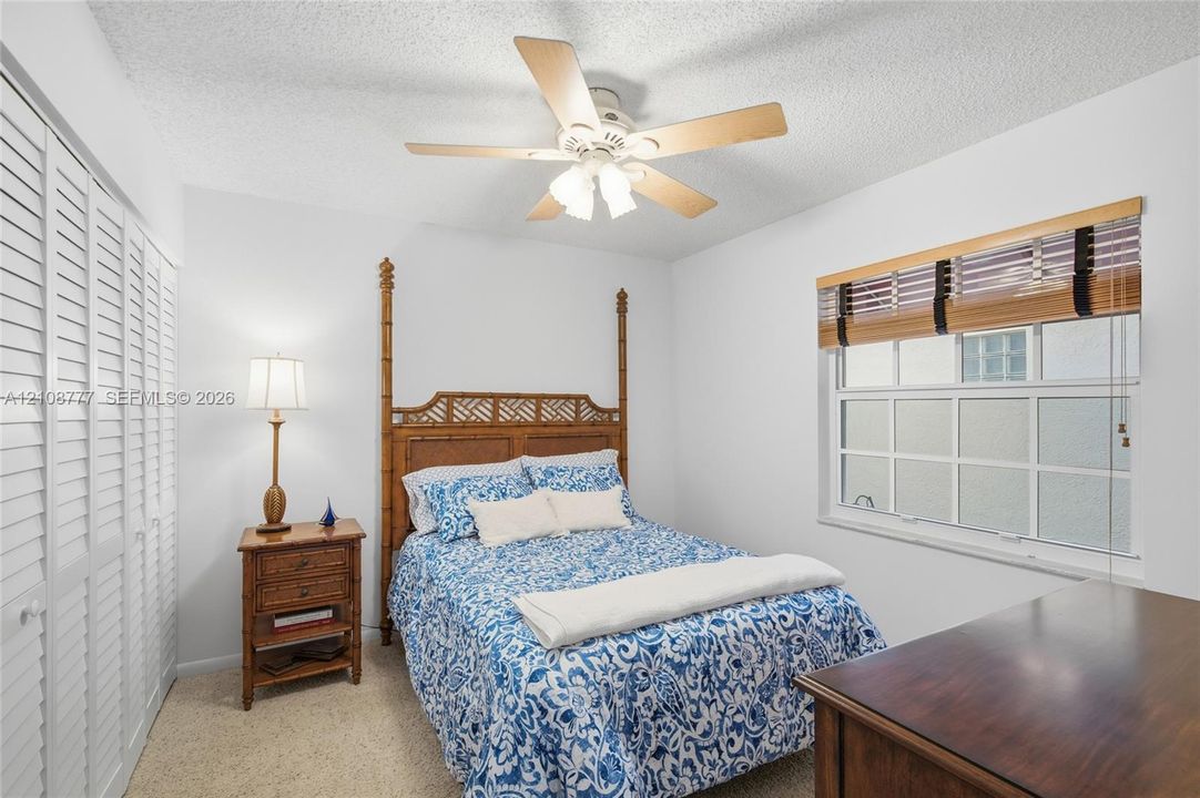 Bedroom featuring wall-to-wall louvered closet doors, multi-pane window with wood-slat blinds, textured ceiling, and a central ceiling fan with integrated light fixture
