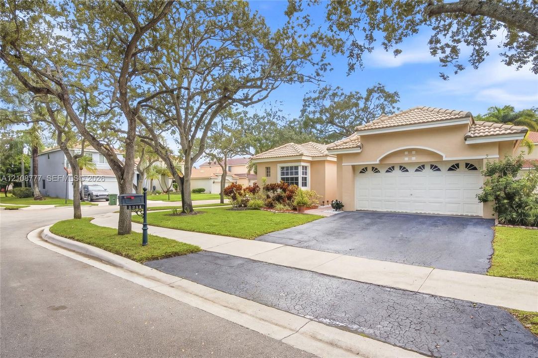 Single-story residence featuring a stucco exterior, a multi-car garage with arched decorative glass detailing, tile roofing, and mature trees
