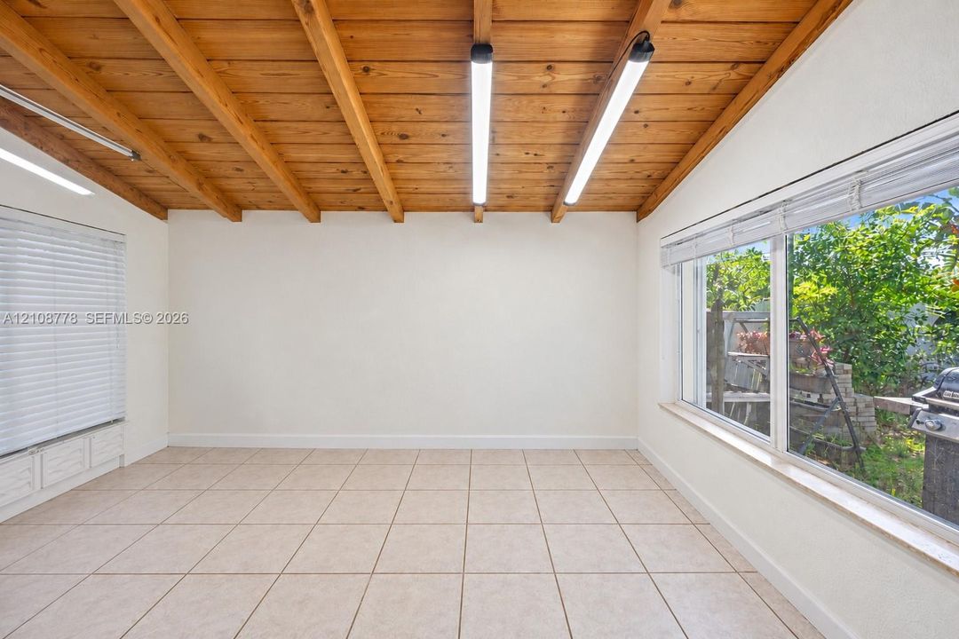 Exposed wood-beam ceiling featuring linear lighting, neutral tile flooring, and large windows with horizontal blinds