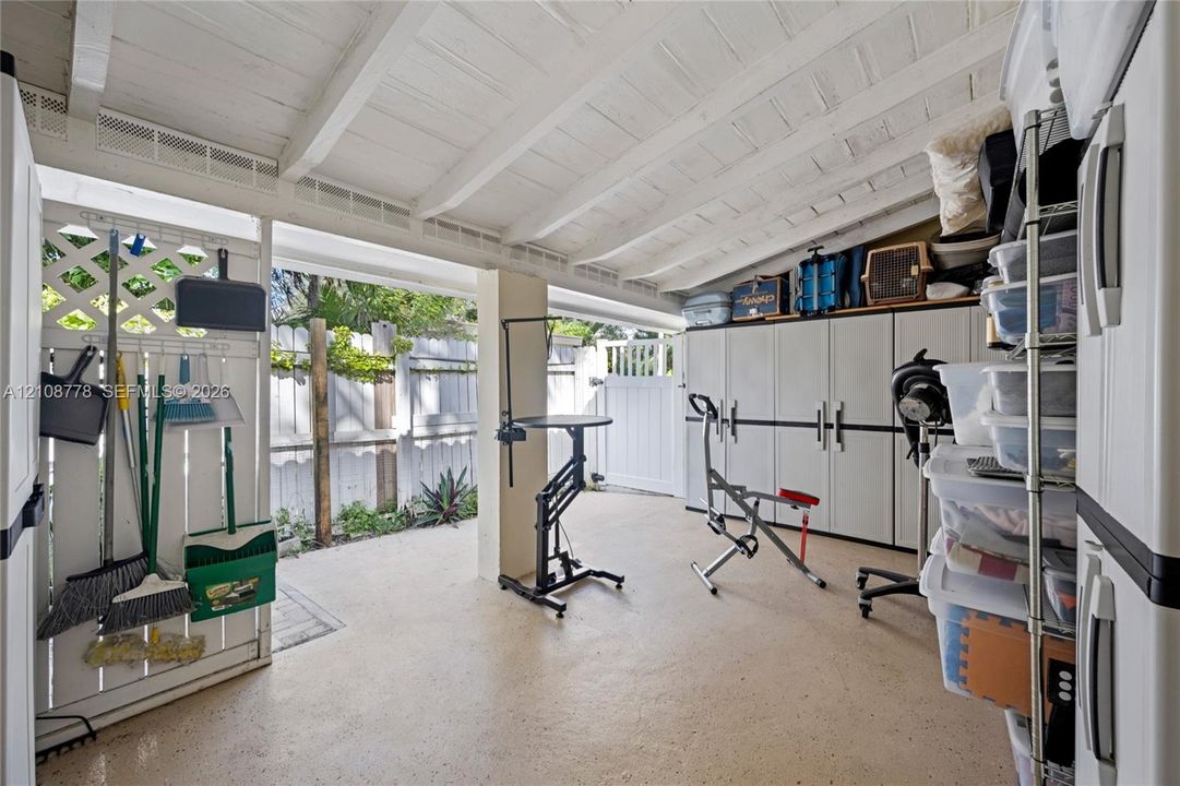 Covered patio area featuring a white-painted exposed beam ceiling, concrete flooring, lattice wall paneling, and a secured gate