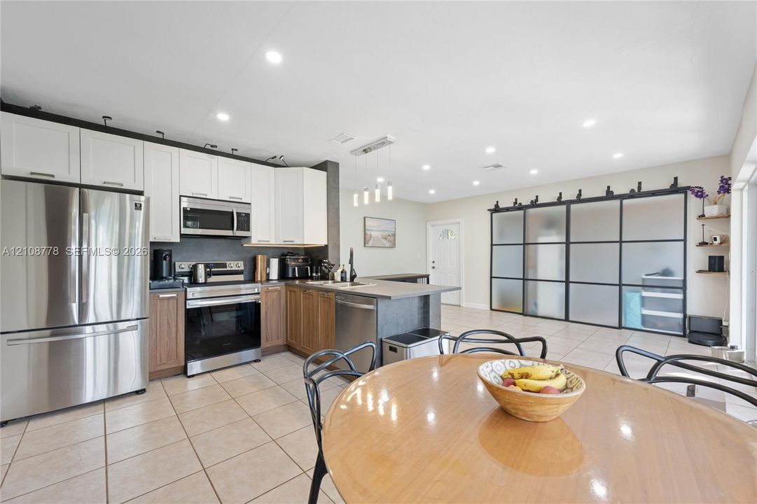 Kitchen featuring dual-tone cabinetry, stainless steel appliances, a peninsula with stone-surface countertop, recessed lighting, and large frosted-glass sliding doors with metal framing
