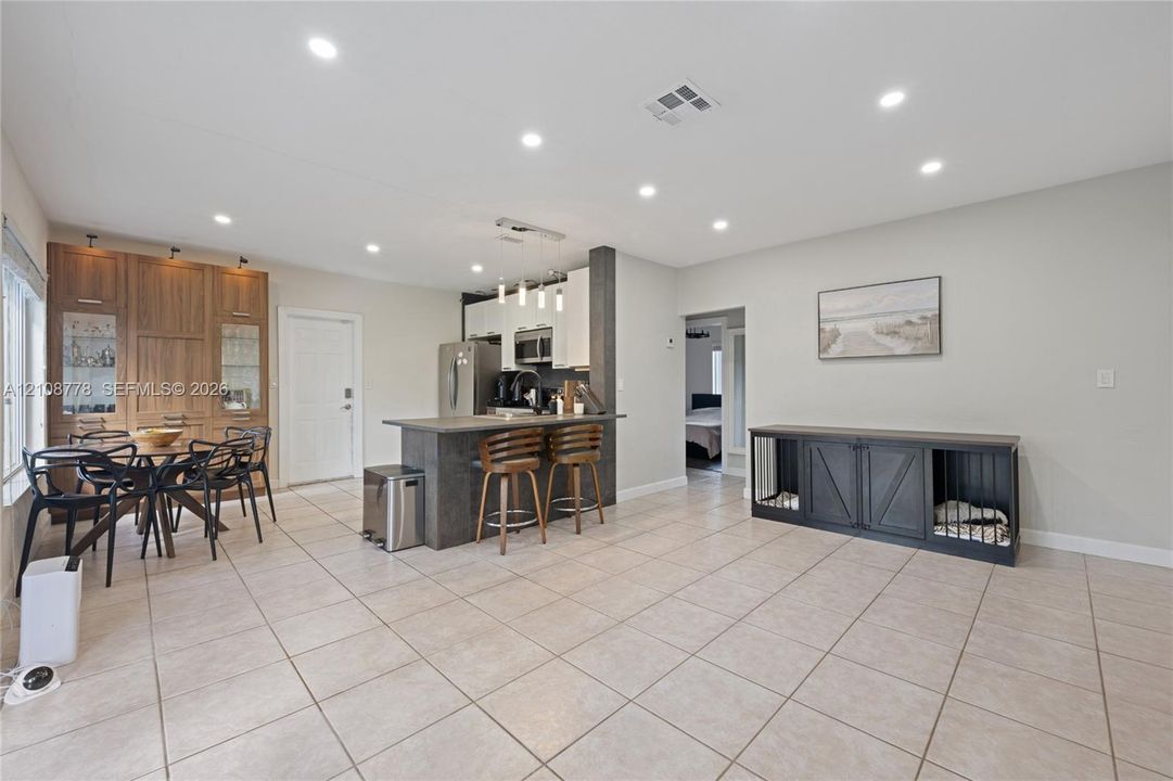 Open-concept kitchen featuring a stone-toppe island with pendant lighting, integrated wood-finish cabinetry, recessed ceiling lights, and tile flooring throughout