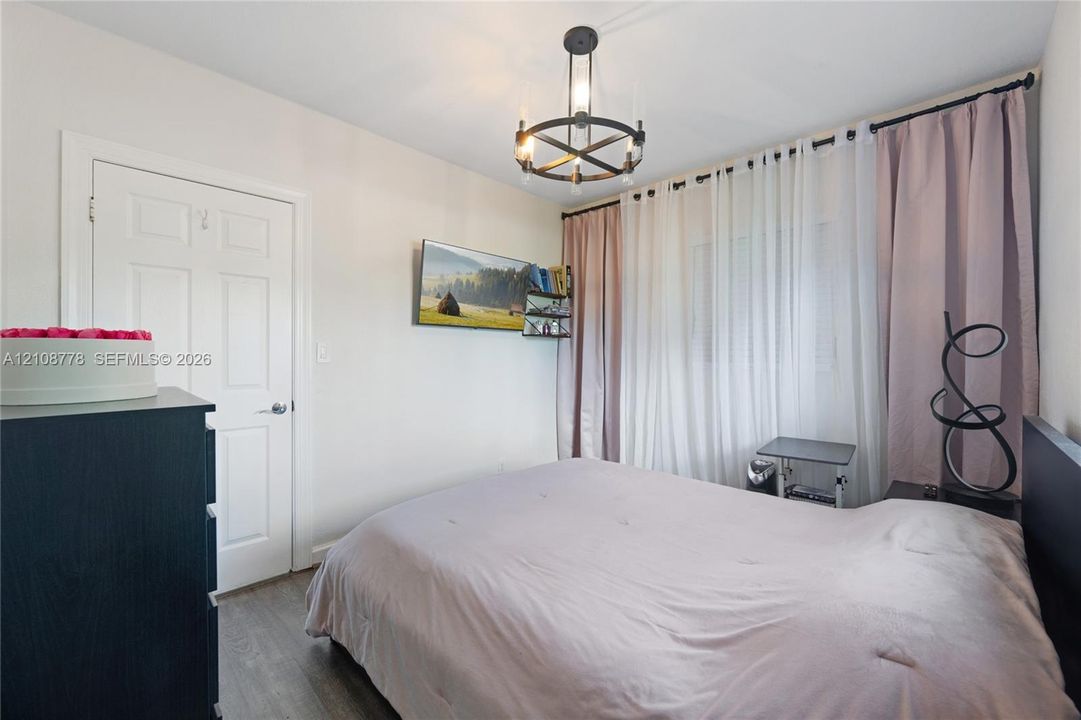 Room featuring wood-finish flooring, a matte black circular chandelier with exposed bulbs, and a six-panel interior door