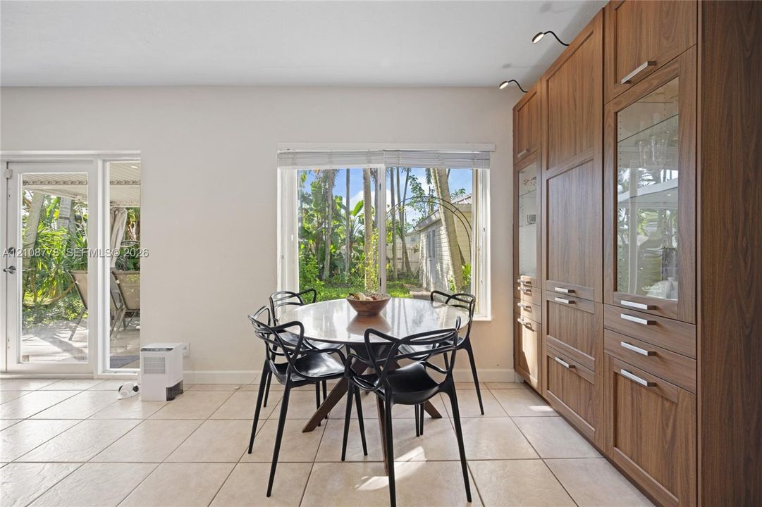 Full-wall wood cabinetry featuring integrated storage, glass-front display sections, and overhead directional lighting, complemented by tile flooring, a large picture window, and a glass-panel exterior door