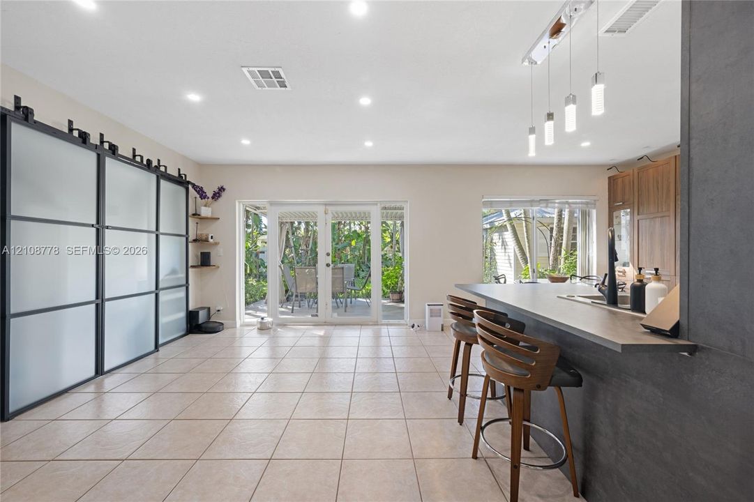 Large-format tile flooring, oversized matte black sliding partition with frosted glass panels, kitchen island with breakfast bar seating, and linear pendant lighting