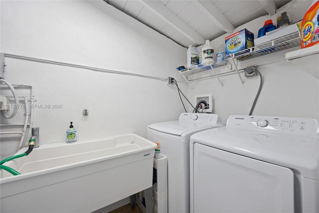 Laundry area featuring a utility sink, exposed painted wood ceiling beams, and integrated wire shelving