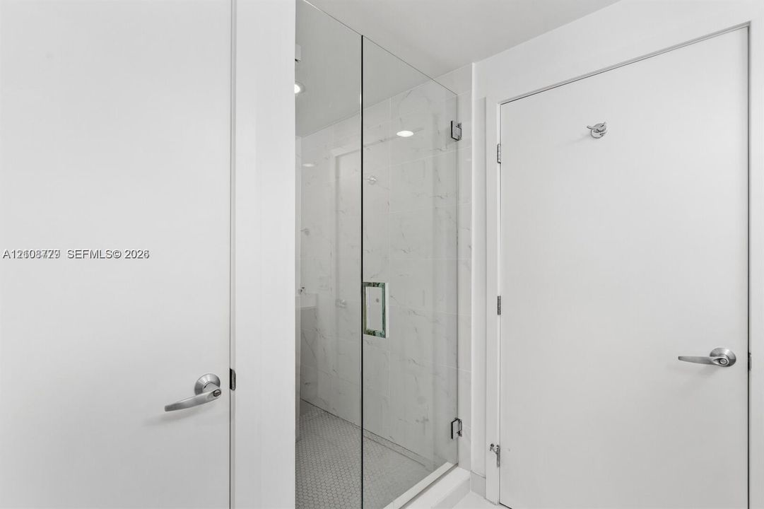 Walk-in shower featuring a frameless glass door, light-toned stone-finish tile surround, and mosaic floor tiling