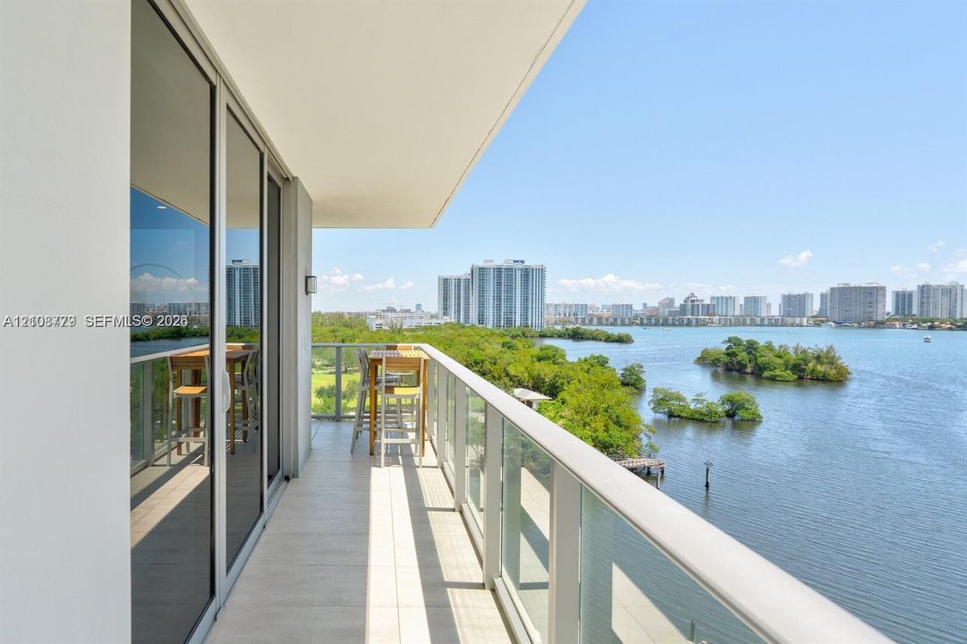 Covered terrace with tile flooring and a glass panel railing, featuring expansive water and skyline scenery