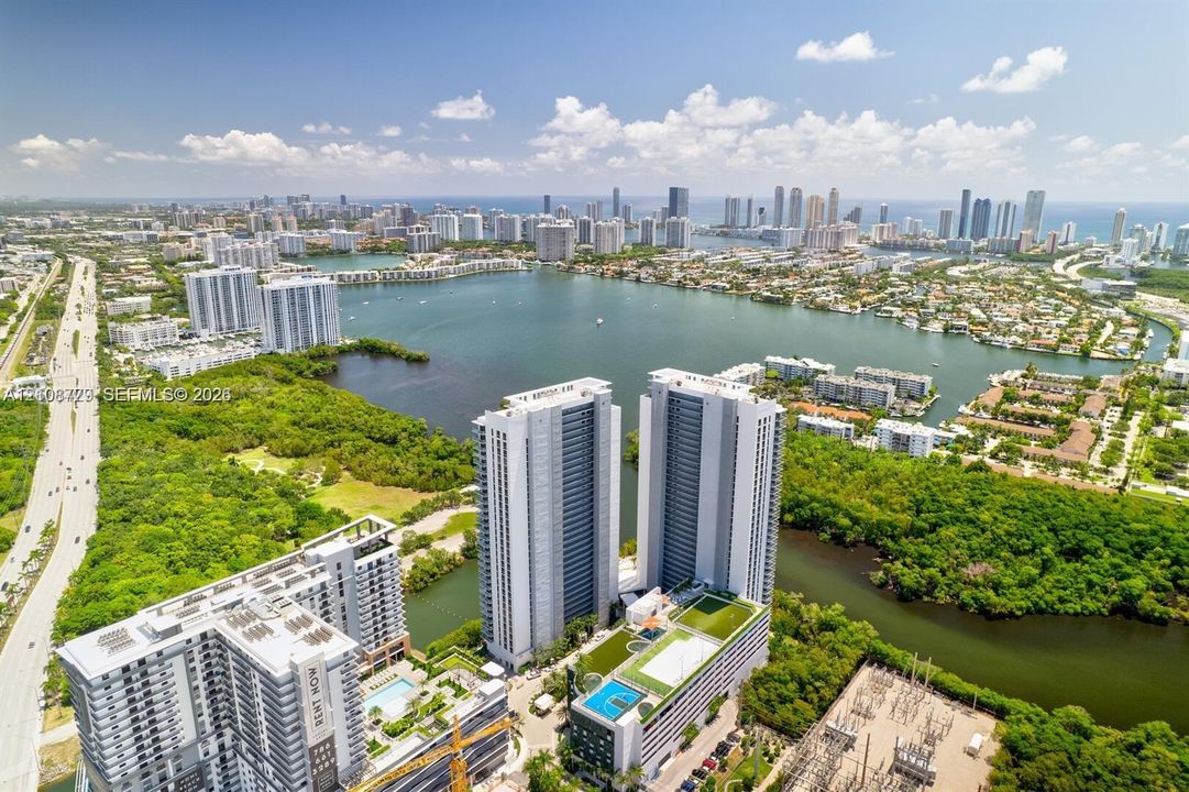 Aerial perspective of high-rise towers featuring rooftop swimming pools, manicured green space, and surrounding water frontage