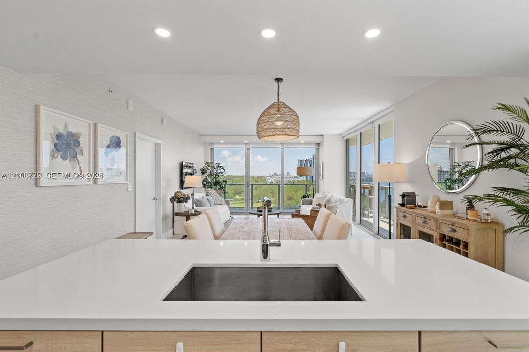 Kitchen island featuring a solid-surface countertop, under-mount stainless steel sink, and light wood-finish cabinetry, complemented by recessed ceiling lighting and floor-to-ceiling glass sliding doors
